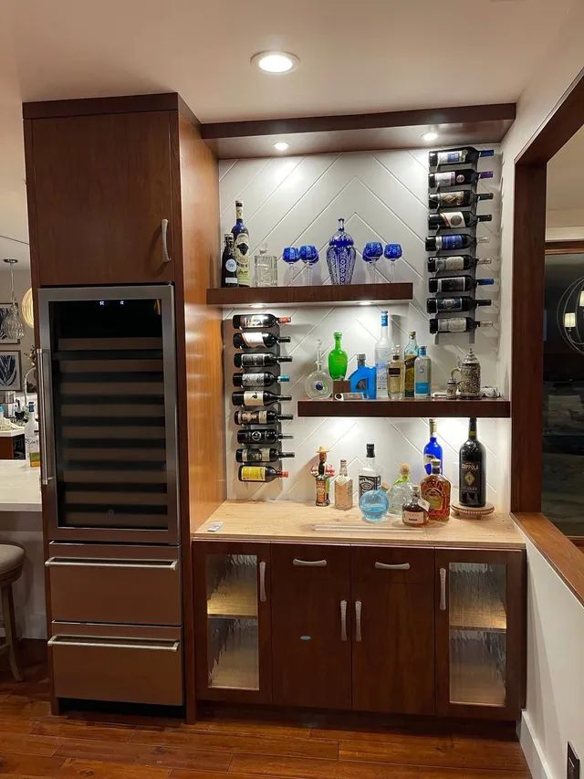 Built-in home bar with wine fridge, shelves, bottles, glasses, and warm wood cabinetry
