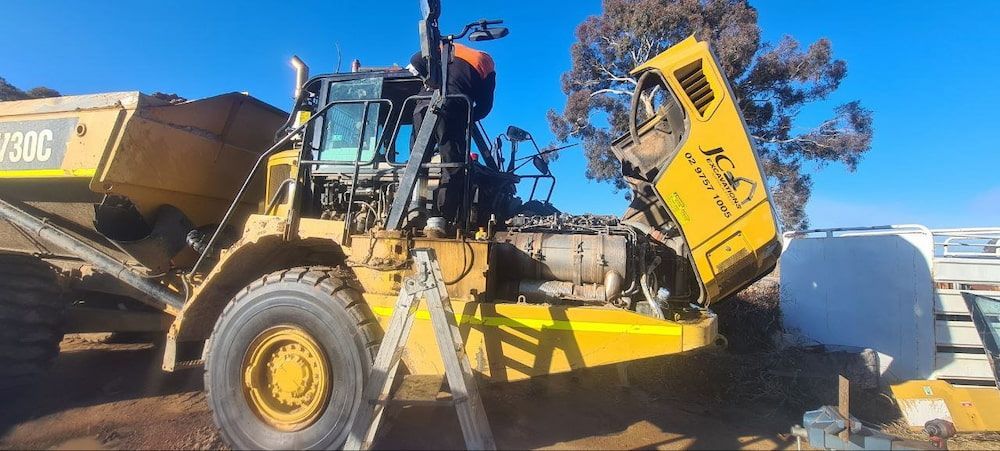 A Yellow Dump Truck With Its Hood Up is Parked in the Dirt — MJR Auto Glass In Southern Highlands, NSW