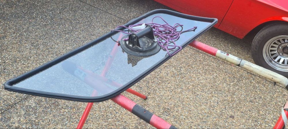 A Broken Windshield is Sitting on a Stand Next to a Red Car — MJR Auto Glass In Southern Highlands, NSW