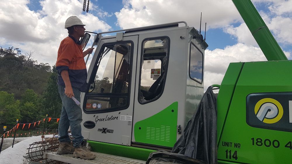 A Man in a Hard Hat is Standing Next to a Green and White Crane — MJR Auto Glass In Bowral, NSW