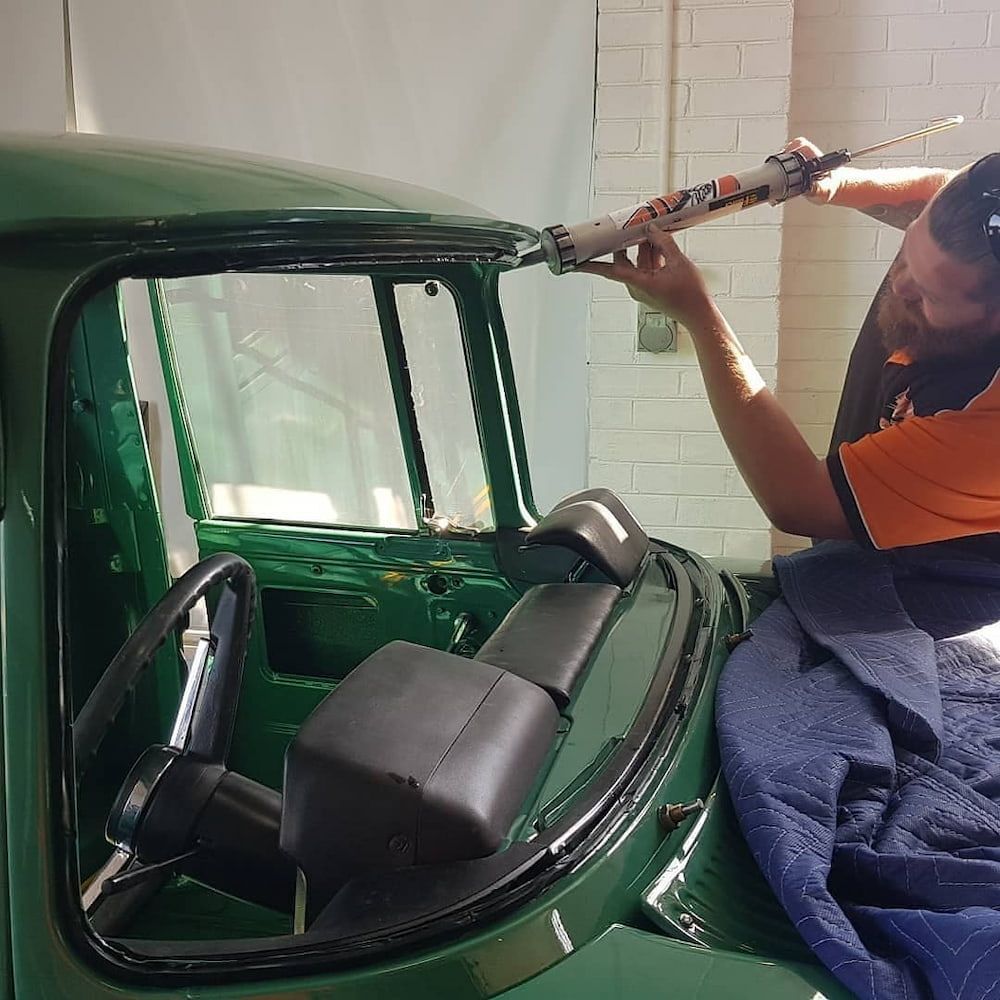 A Man is Installing a Windshield on a Green Truck — MJR Auto Glass In Moss Vale, NSW