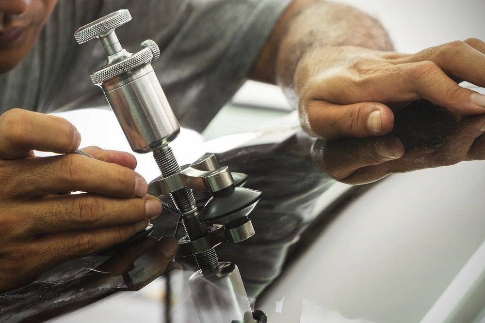 A Man is Working on a Car Windshield With a Tool — MJR Auto Glass In Canberra, ACT