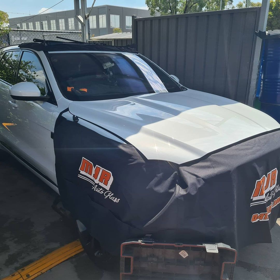 A White Car With A Black Cover On The Hood Is Parked In A Parking Lot — MJR Auto Glass In Goulburn, NSW