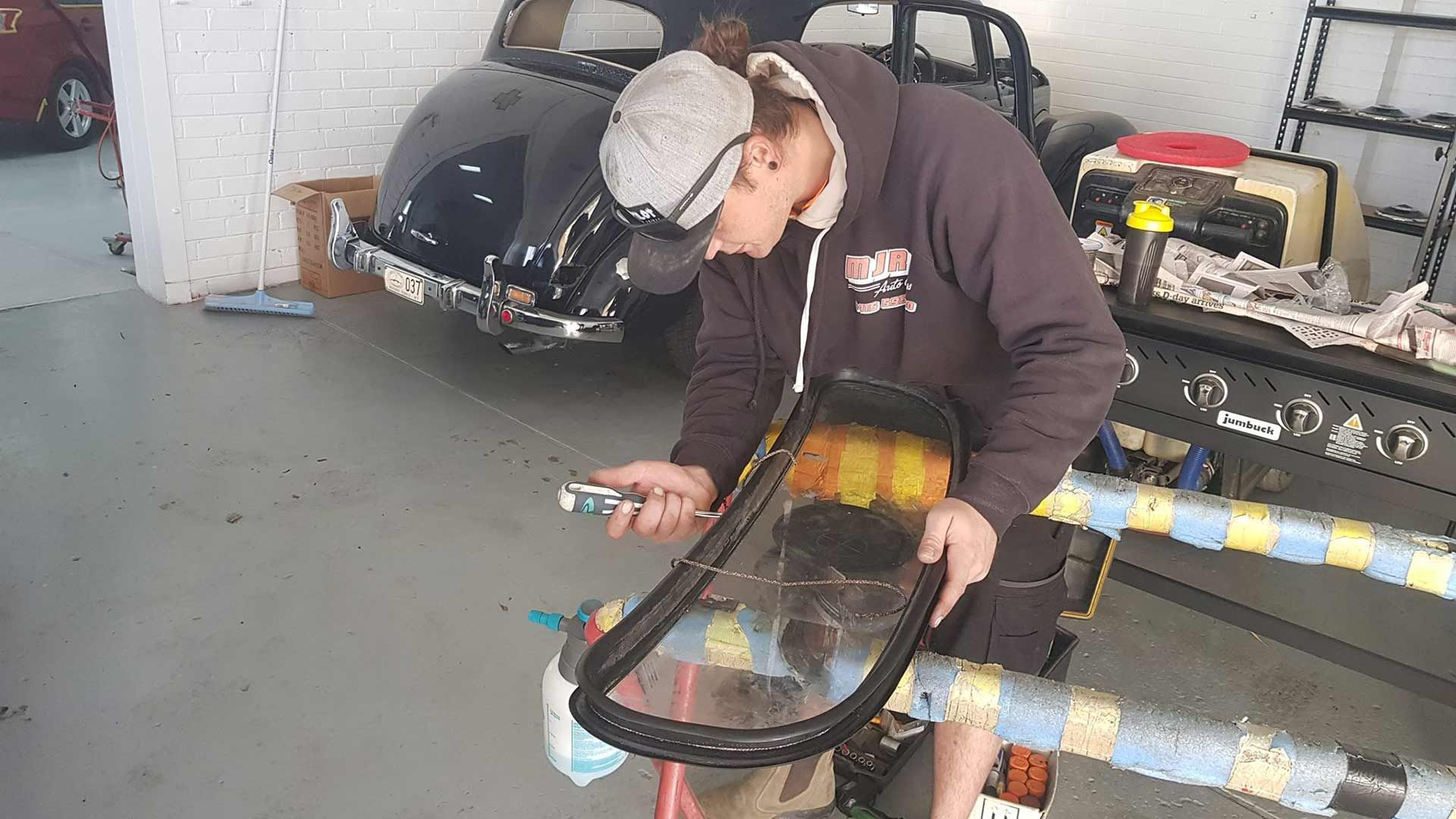 A Man Is Working On A Car Windshield In A Garage — MJR Auto Glass In Goulburn, NSW