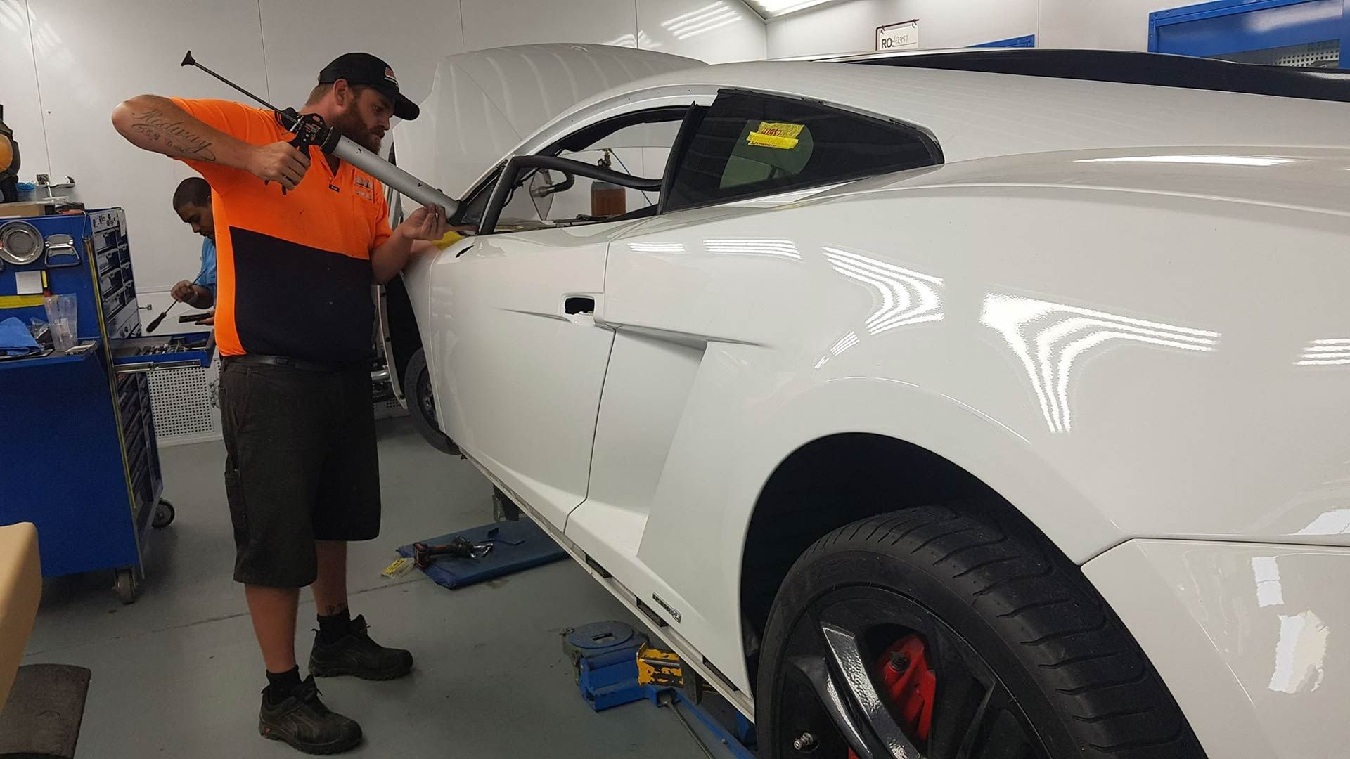 A Man Is Working On A White Sports Car In A Garage — MJR Auto Glass In Goulburn, NSW