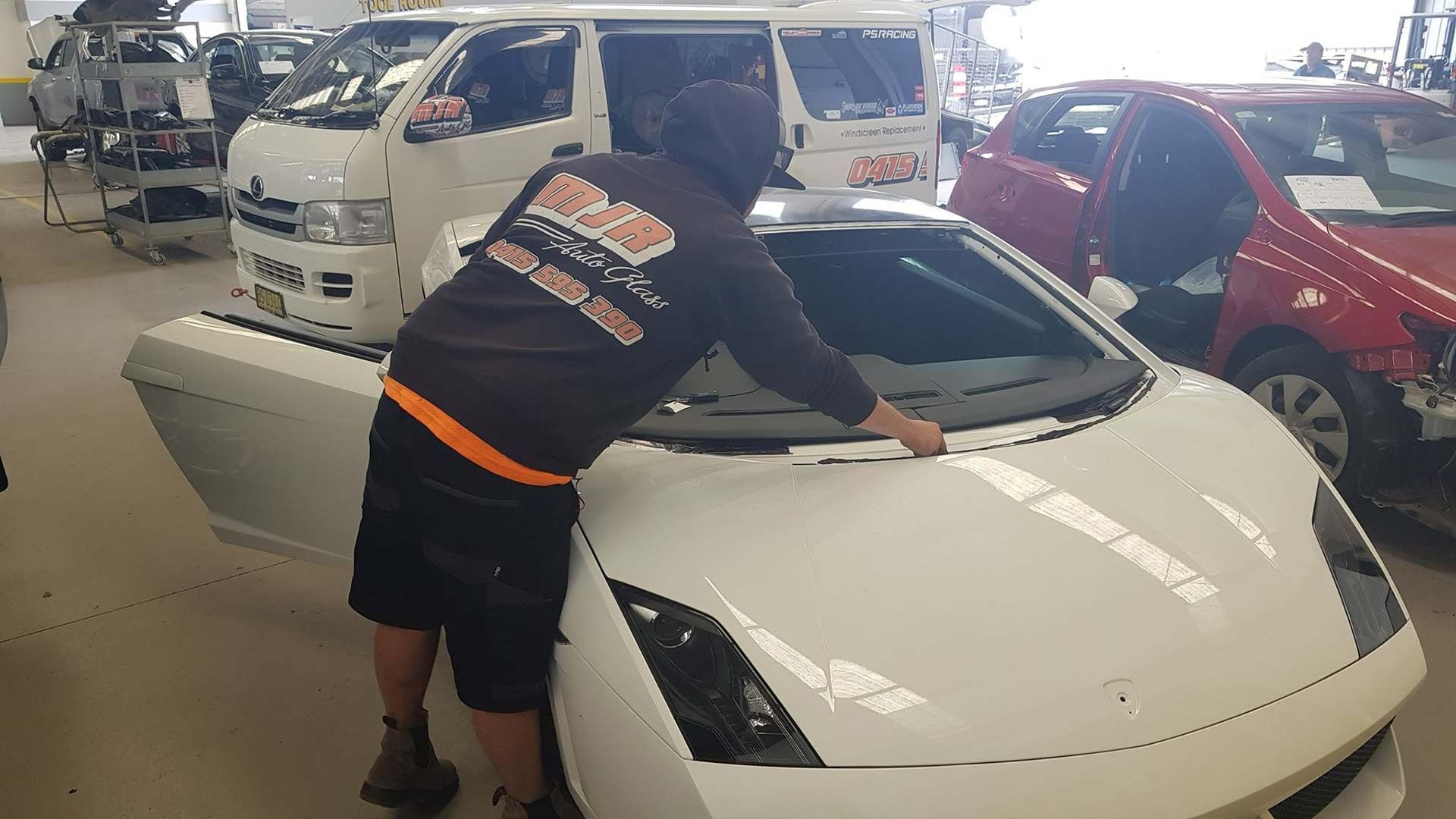 A Man Is Working On A White Sports Car In A Garage — MJR Auto Glass In Goulburn, NSW