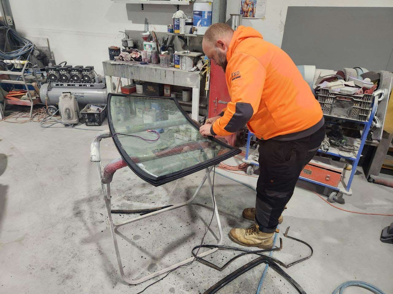 A Man Is Working On A Windshield In A Garage — MJR Auto Glass In Goulburn, NSW