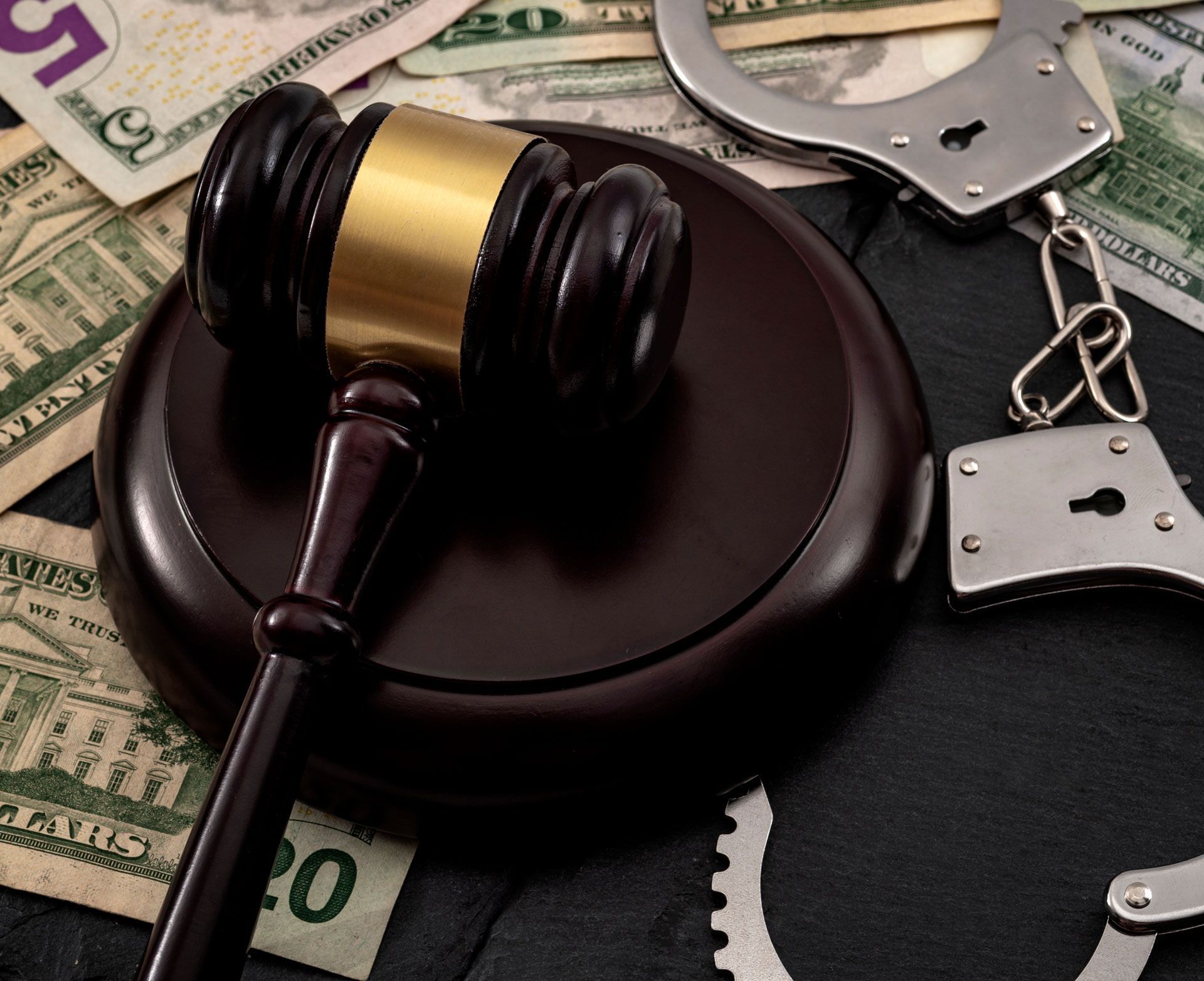 Judge’s gavel on a wooden block beside handcuffs and dollar bills