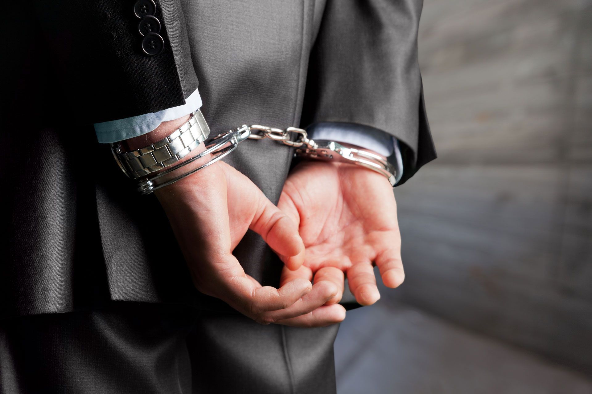 Handcuffed person in a gray suit with hands behind their back
