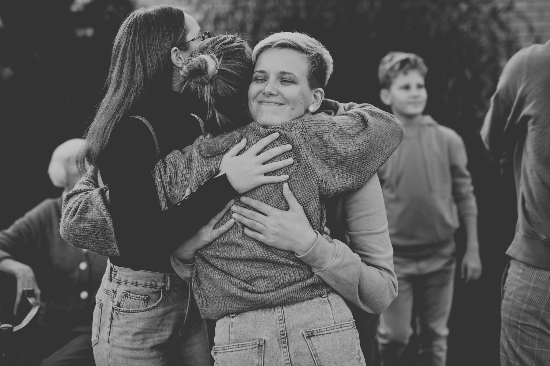 People hugging outdoors, with smiling faces and a blurred crowd in the background