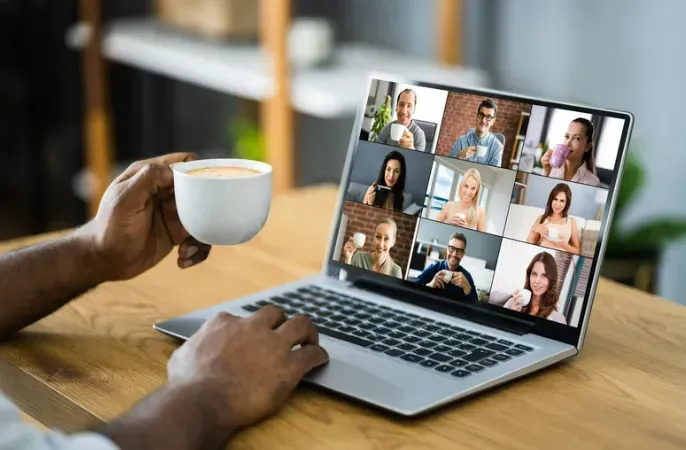 A person is holding a cup of coffee in front of a laptop computer.