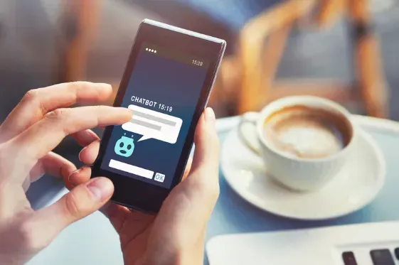 A person is holding a cell phone next to a cup of coffee.