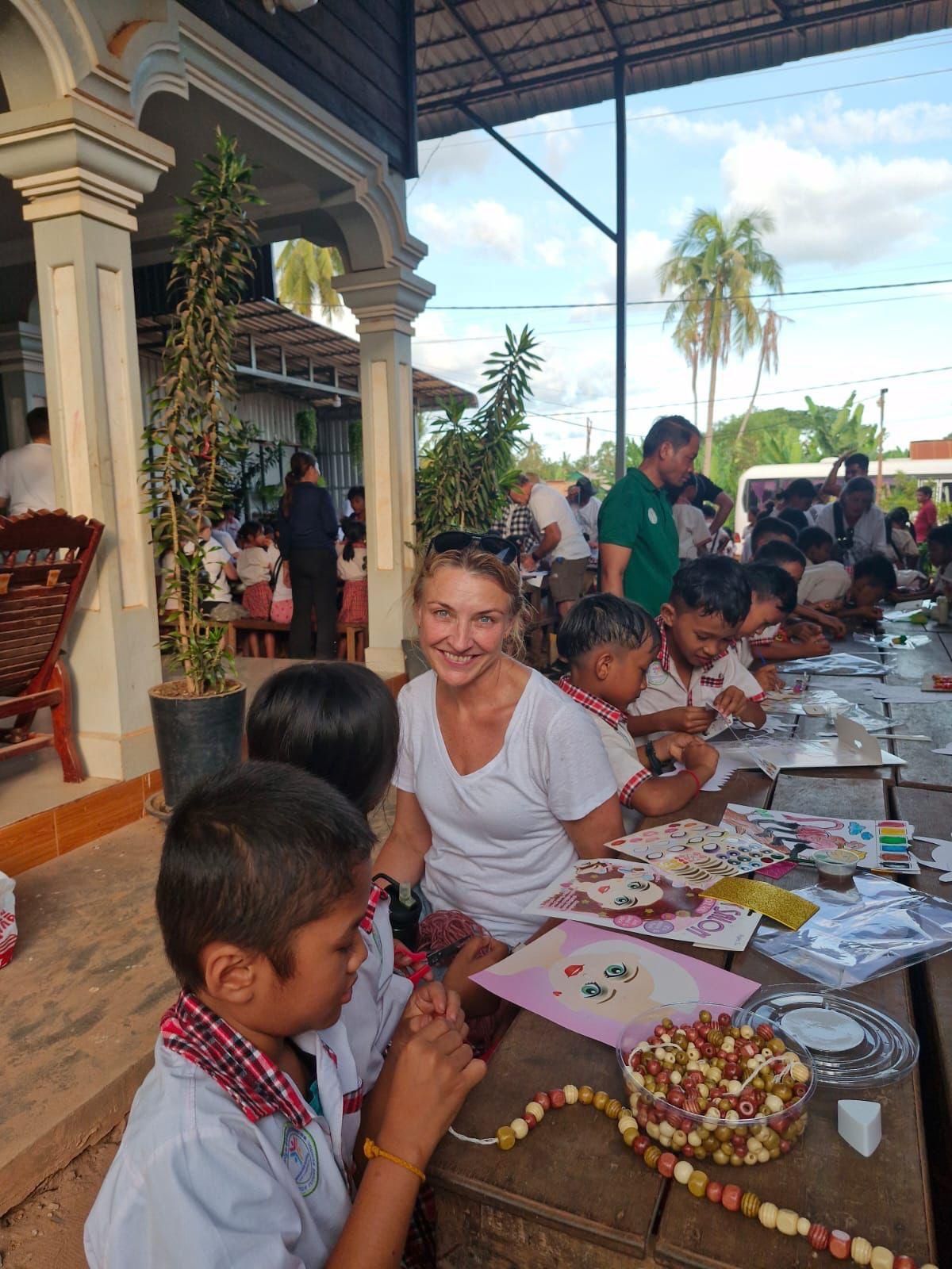 People seated at a long craft table outdoors, making paper decorations under a covered patio.