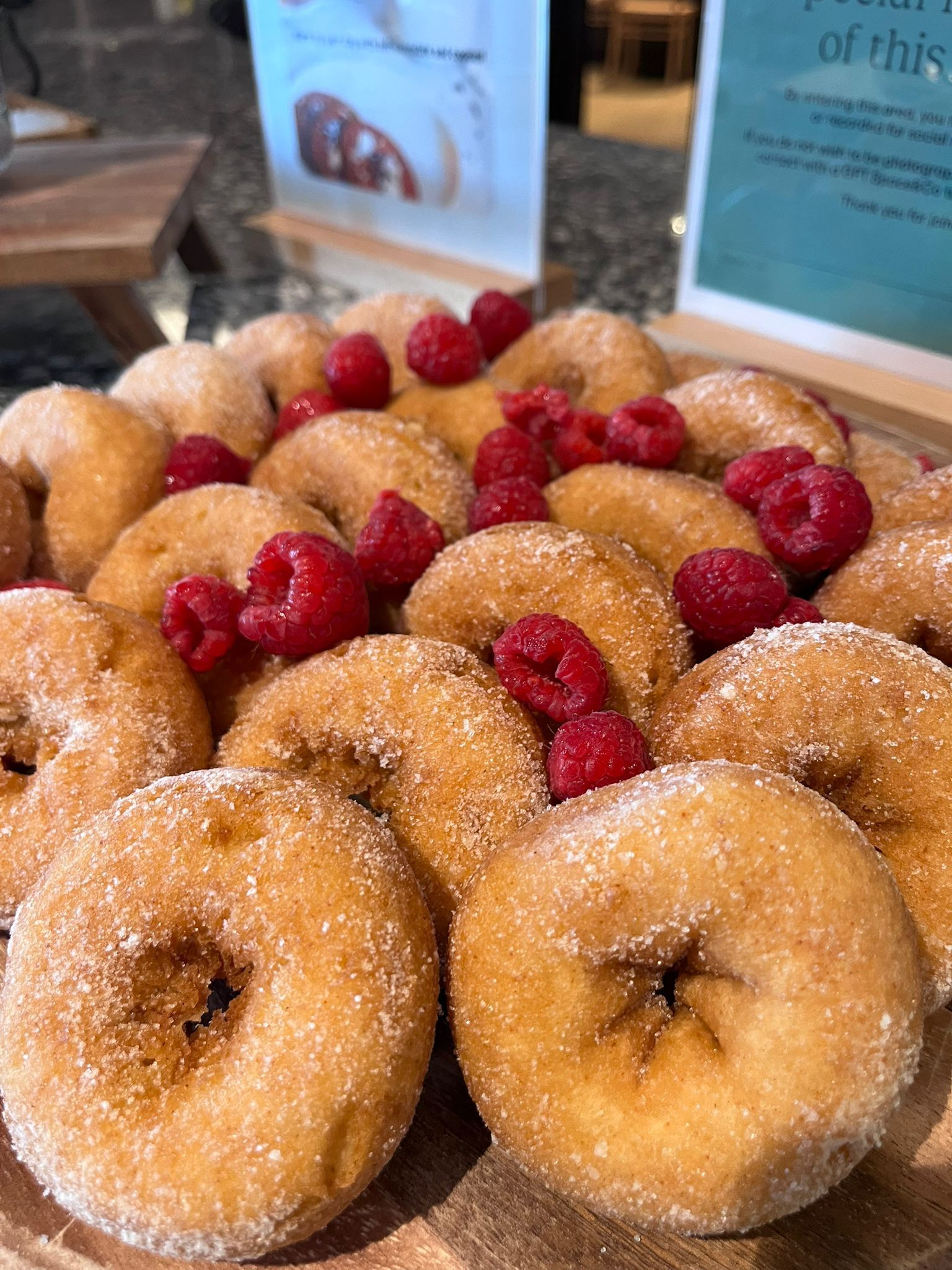 Tray of sugar-dusted donuts topped with raspberries on a bakery display