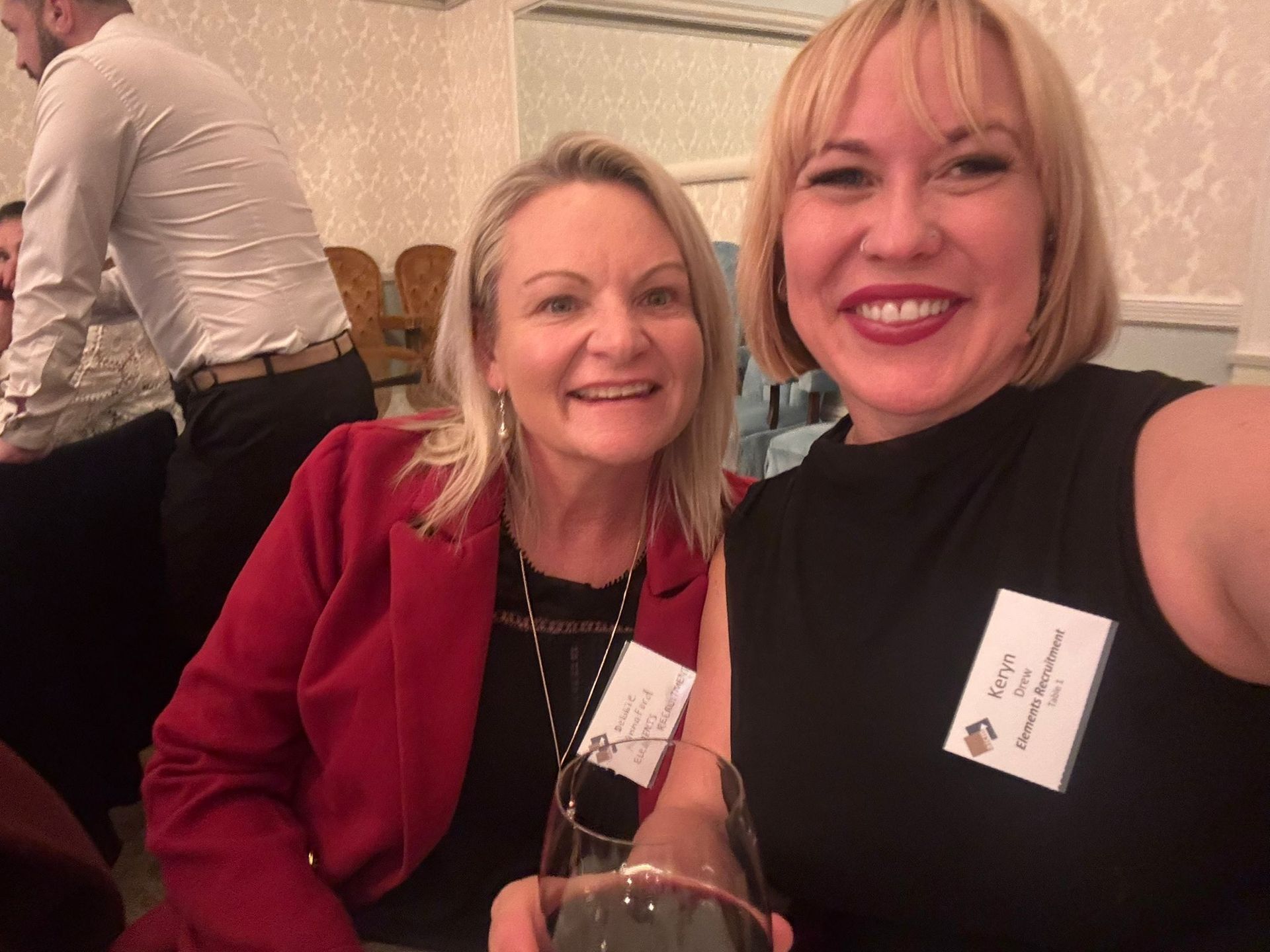 Two women smiling at a table in a warmly lit indoor event setting