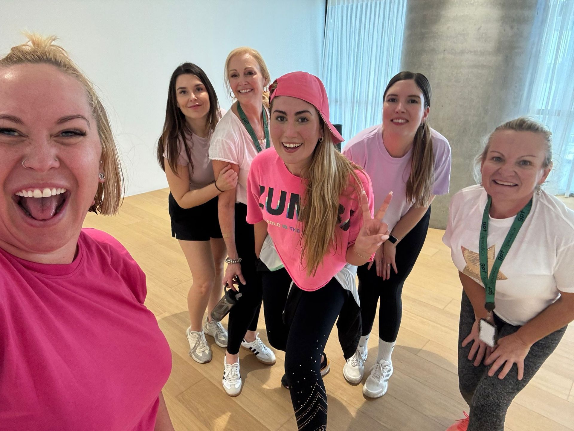 Five people smiling in bright workout clothes pose in a dance studio.