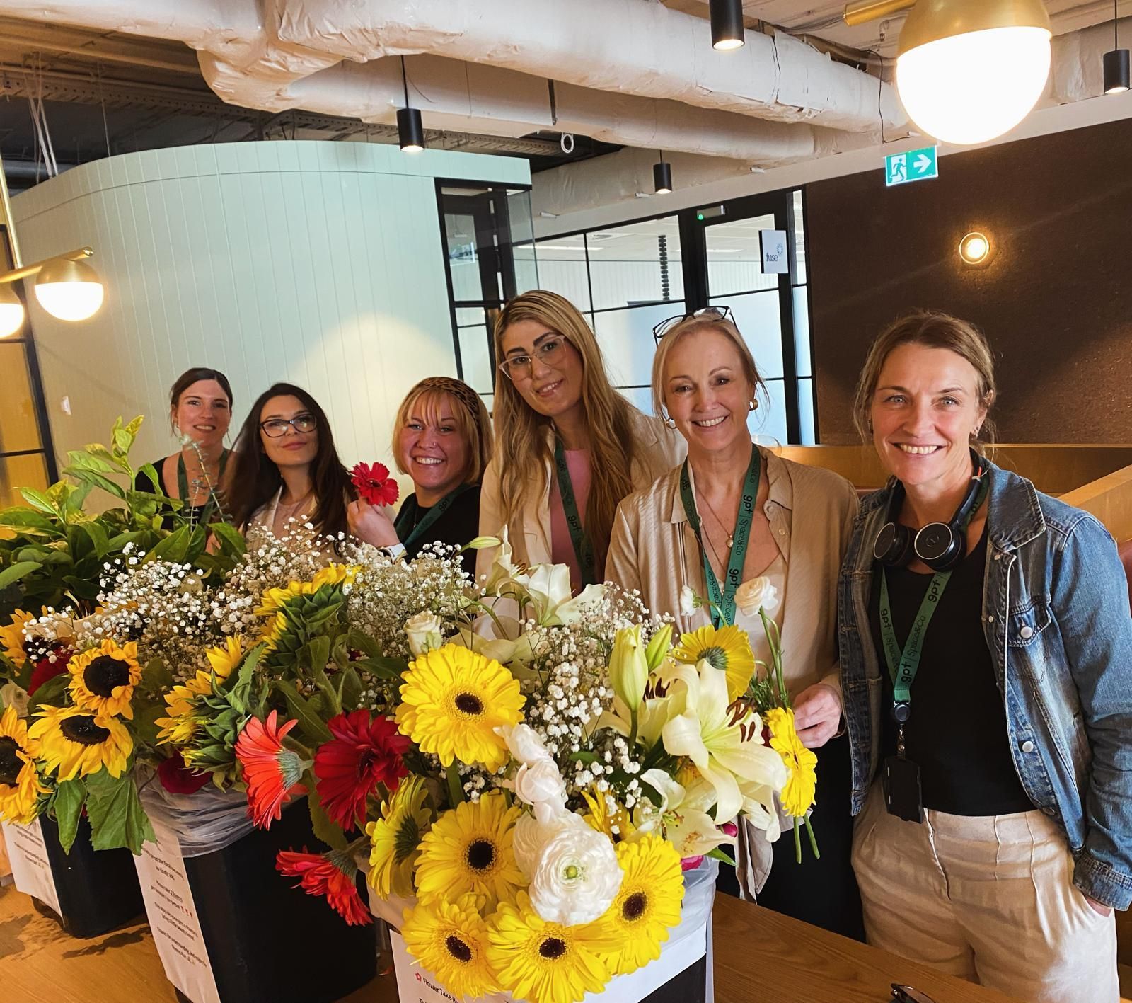 Five people standing behind bouquets of bright sunflowers and mixed flowers in a cozy indoor space