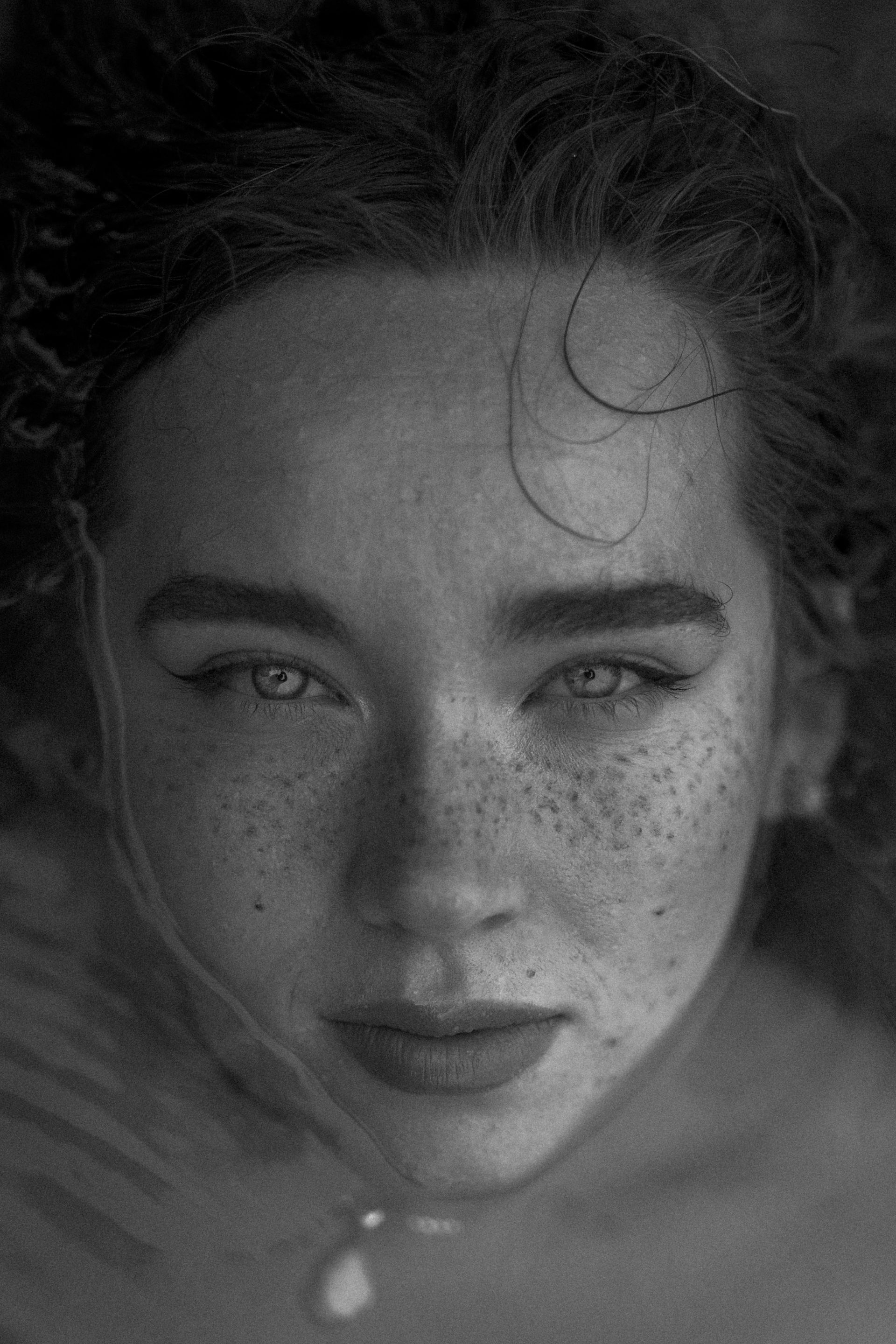 Black-and-white close-up portrait of a person with freckles and intense eyes, hair framing the face.
