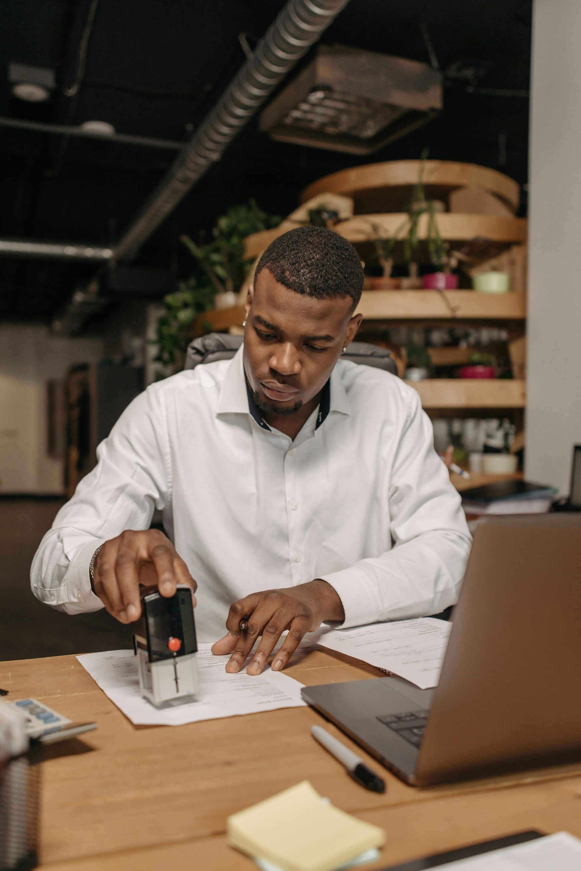 Man stamping paper at a desk with a laptop in a modern office