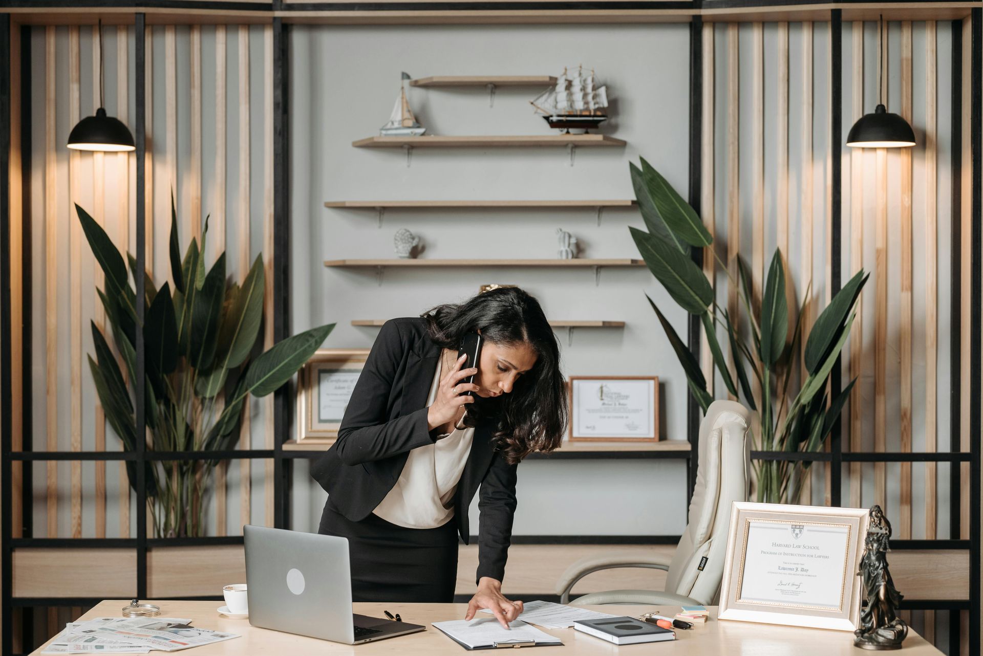 A woman is standing at a desk talking on a cell phone.