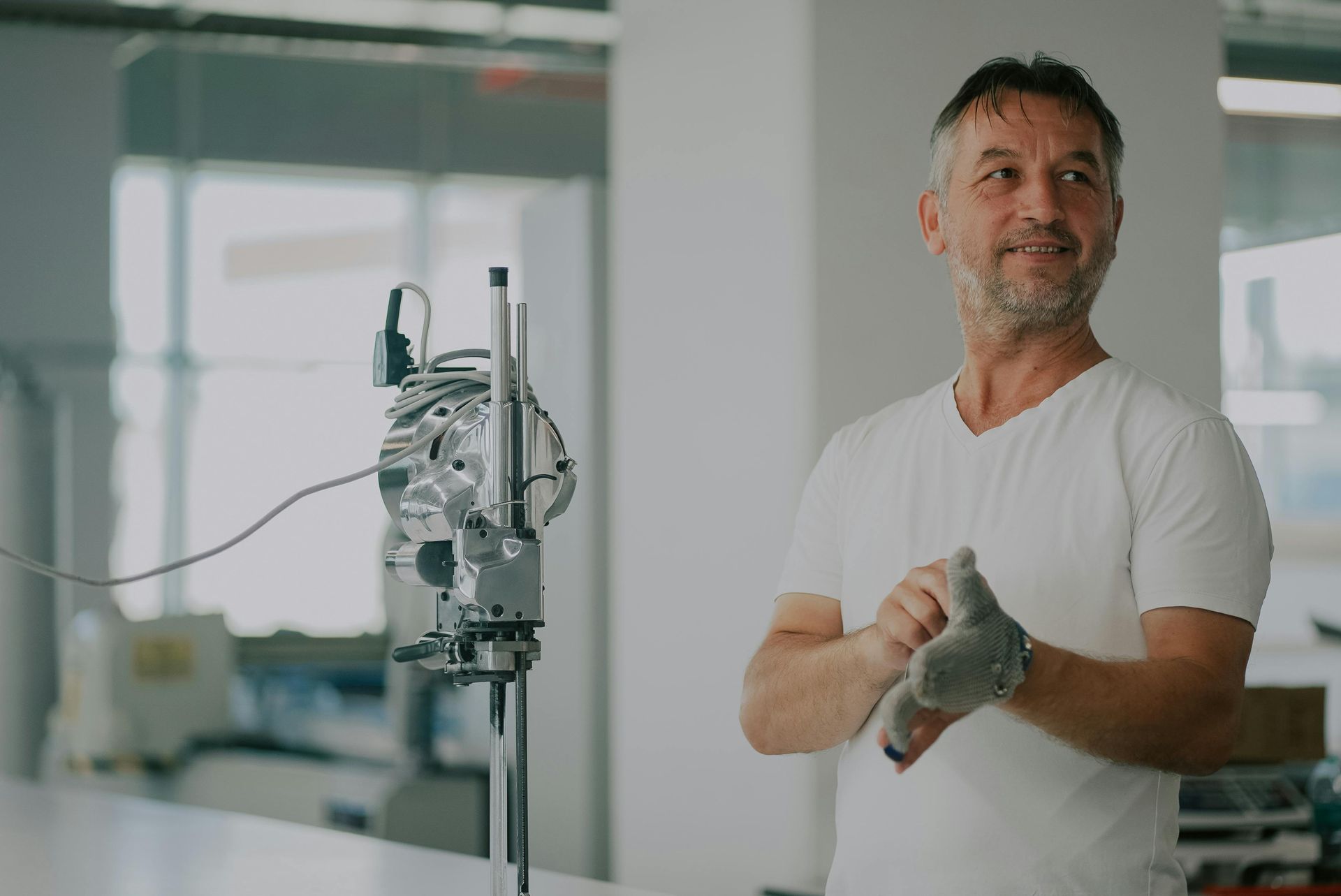 Man in white T-shirt adjusting a medical IV stand in a bright hospital room