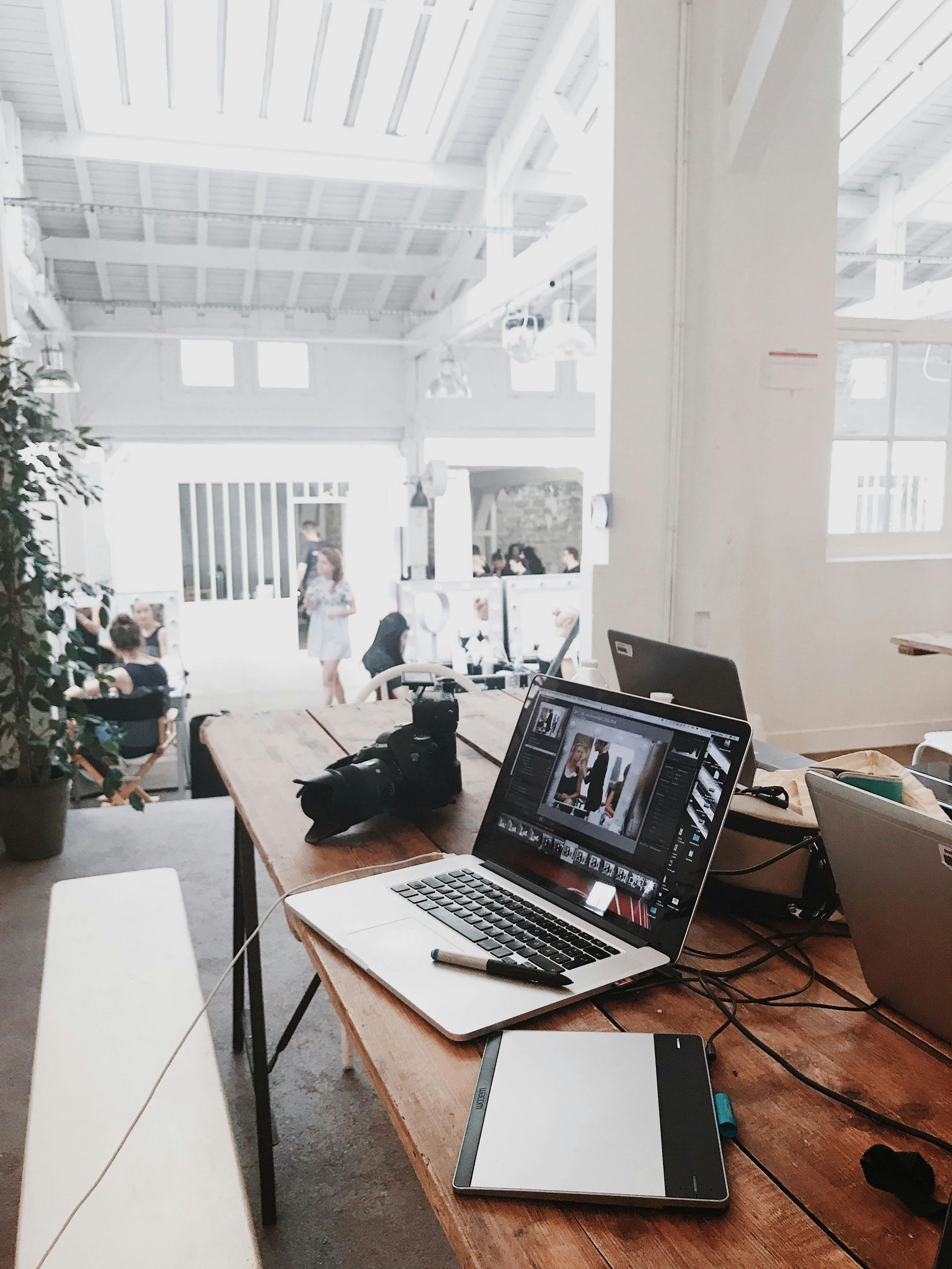 Open laptop on wooden desk in bright loft workspace with cables and notebook.