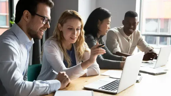 A group of people are sitting at a table looking at laptops.