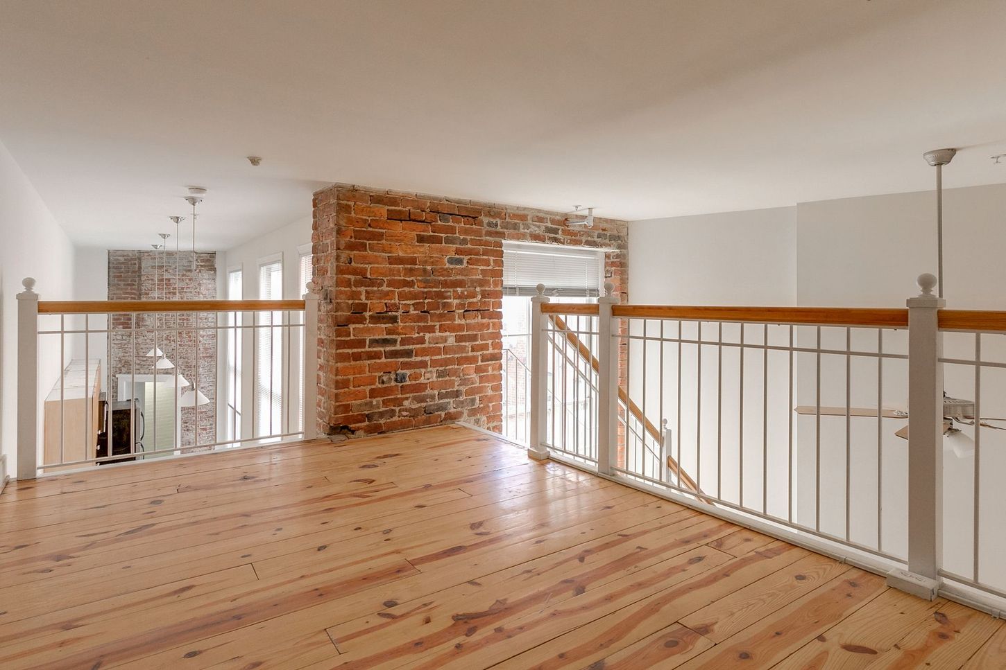 Loft interior with wood floor, brick wall, and white railings.