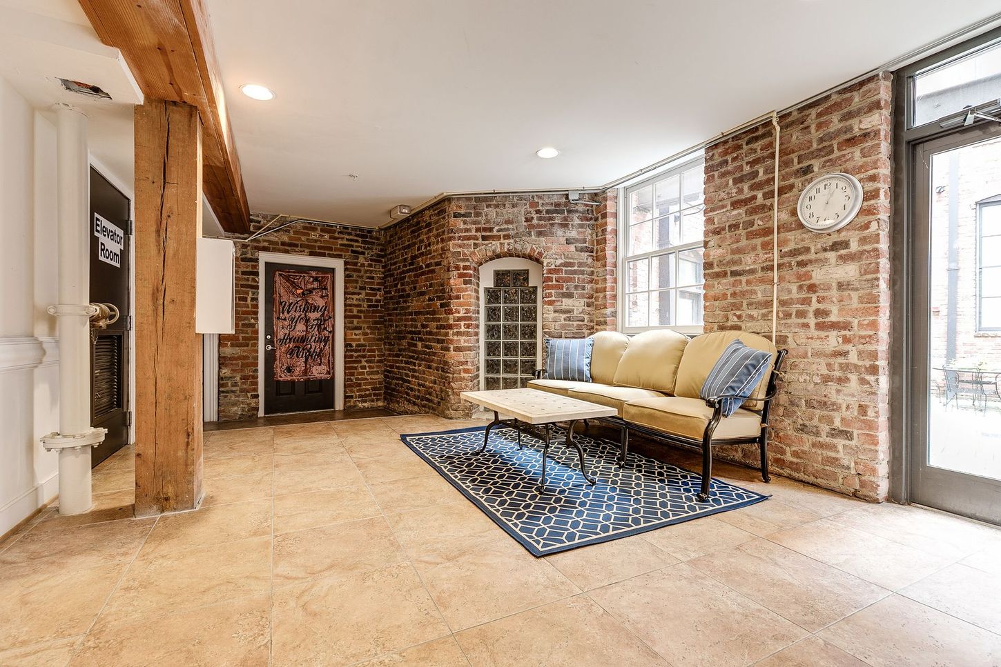 Living room with exposed brick walls, a beige couch, and a blue rug.