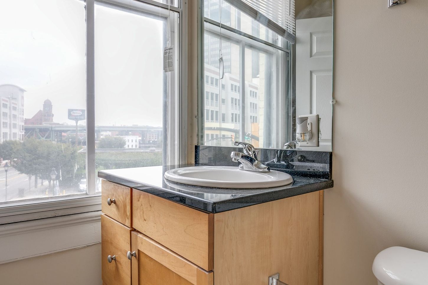 Bathroom with wooden vanity, oval sink, dark countertop, and window with a city view.
