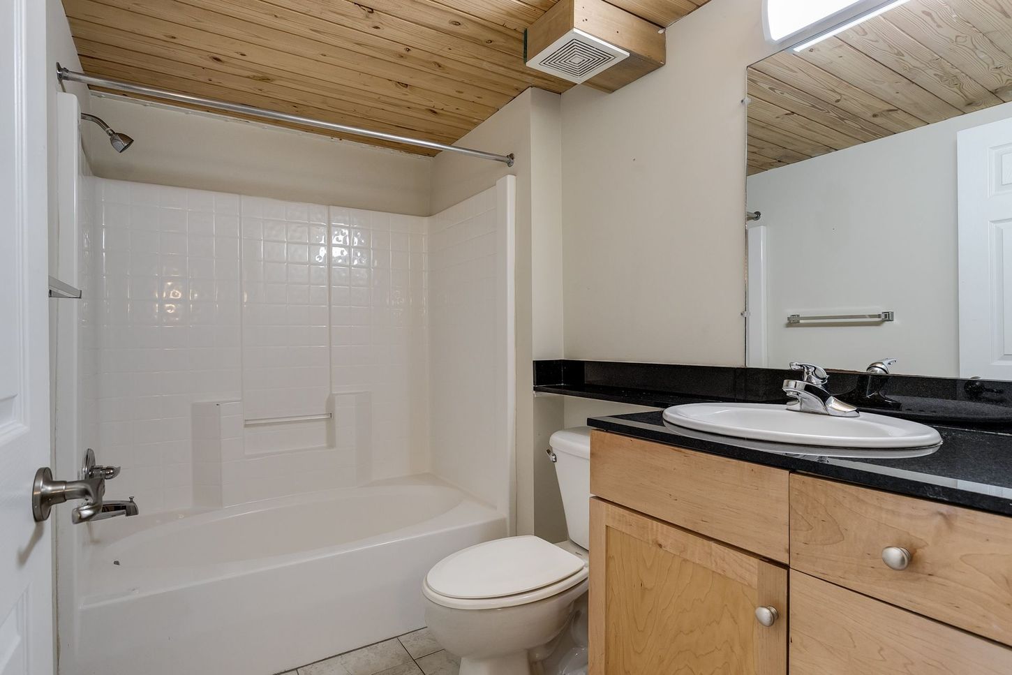 Bathroom with a white tub and toilet, light wood vanity, and a wood ceiling.