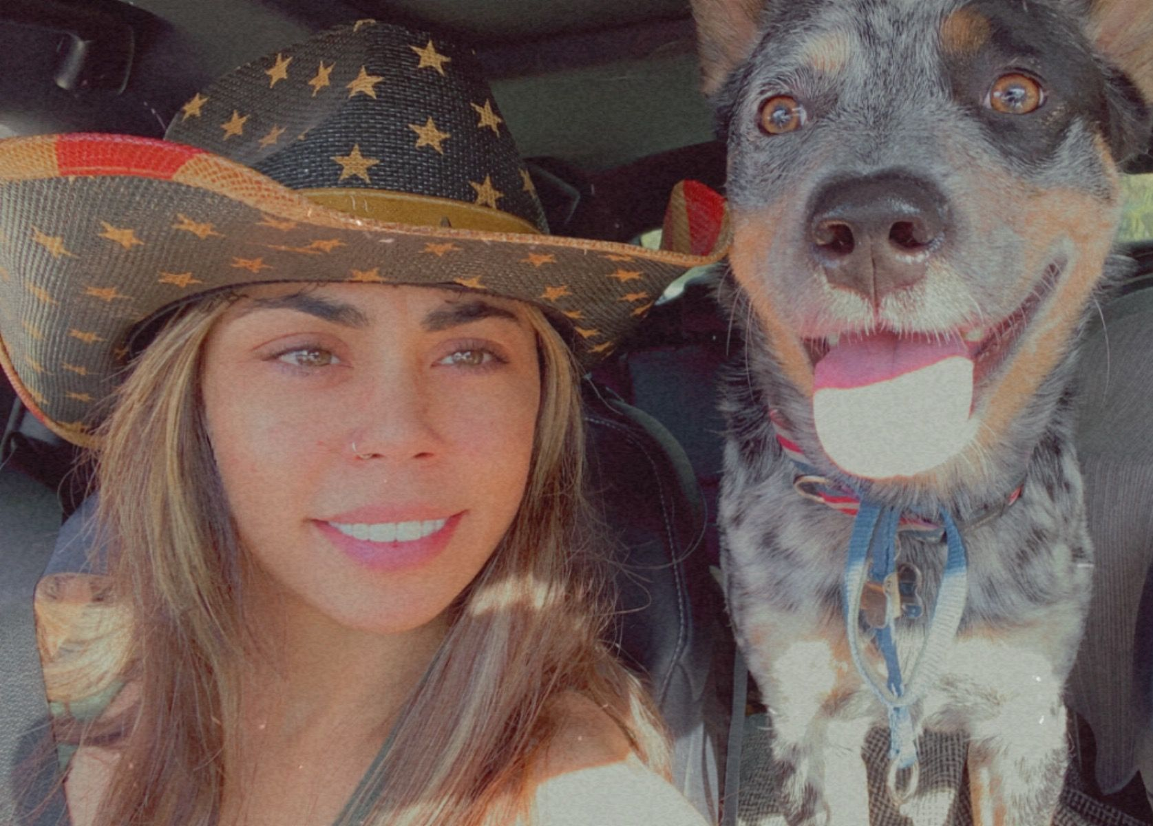 Woman in a star-patterned hat posing beside a black-and-tan dog with tongue out in warm sunlight
