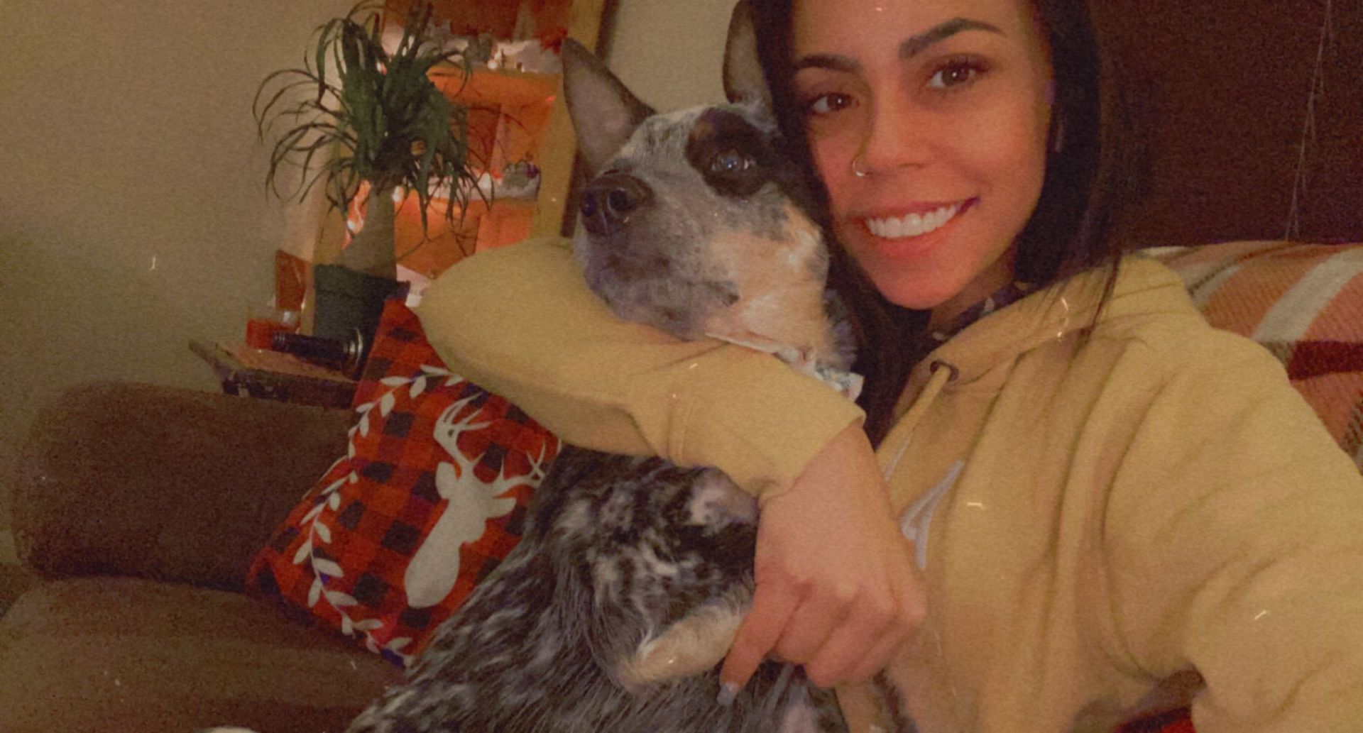 Woman smiling on a couch, hugging a gray dog in a yellow sweater.