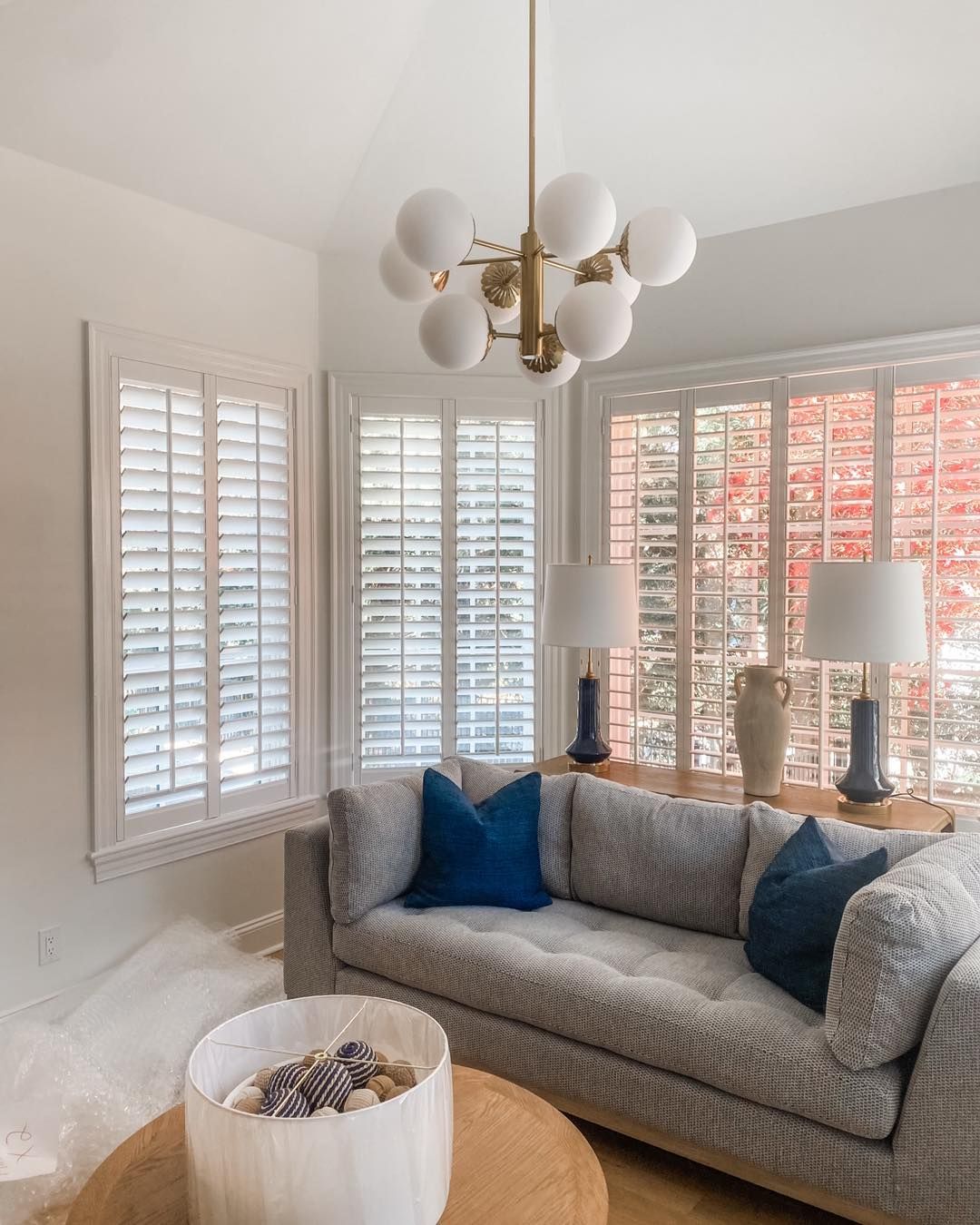 Living room with a gray sofa, blue pillows, white shutters, and a globe chandelier.
