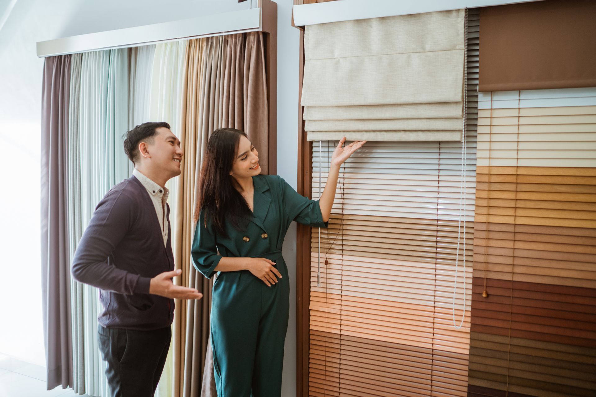 A person is gesturing toward Roman shades in a blind shop display.