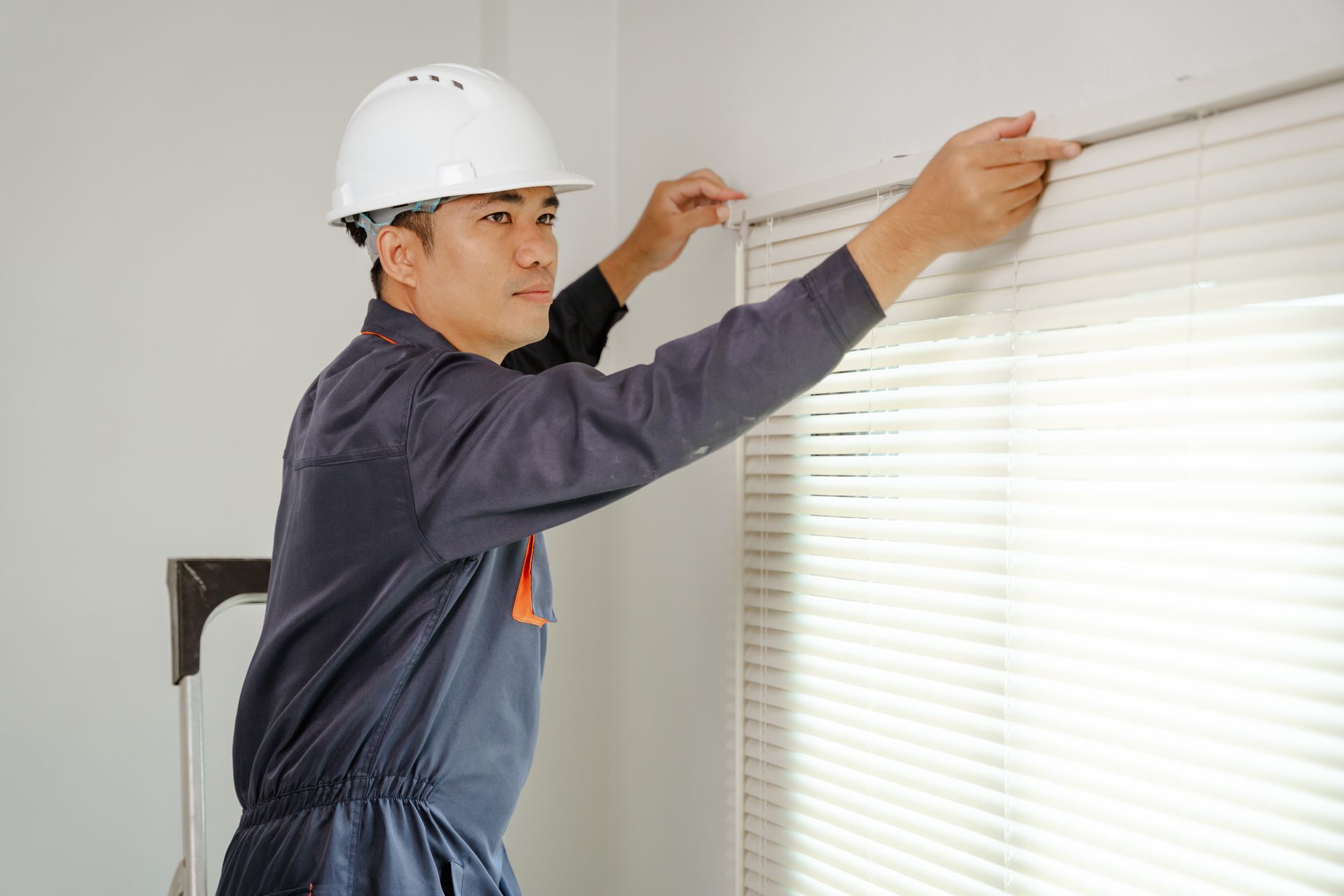 Technician in hard hat adjusting white venetian blinds on a window