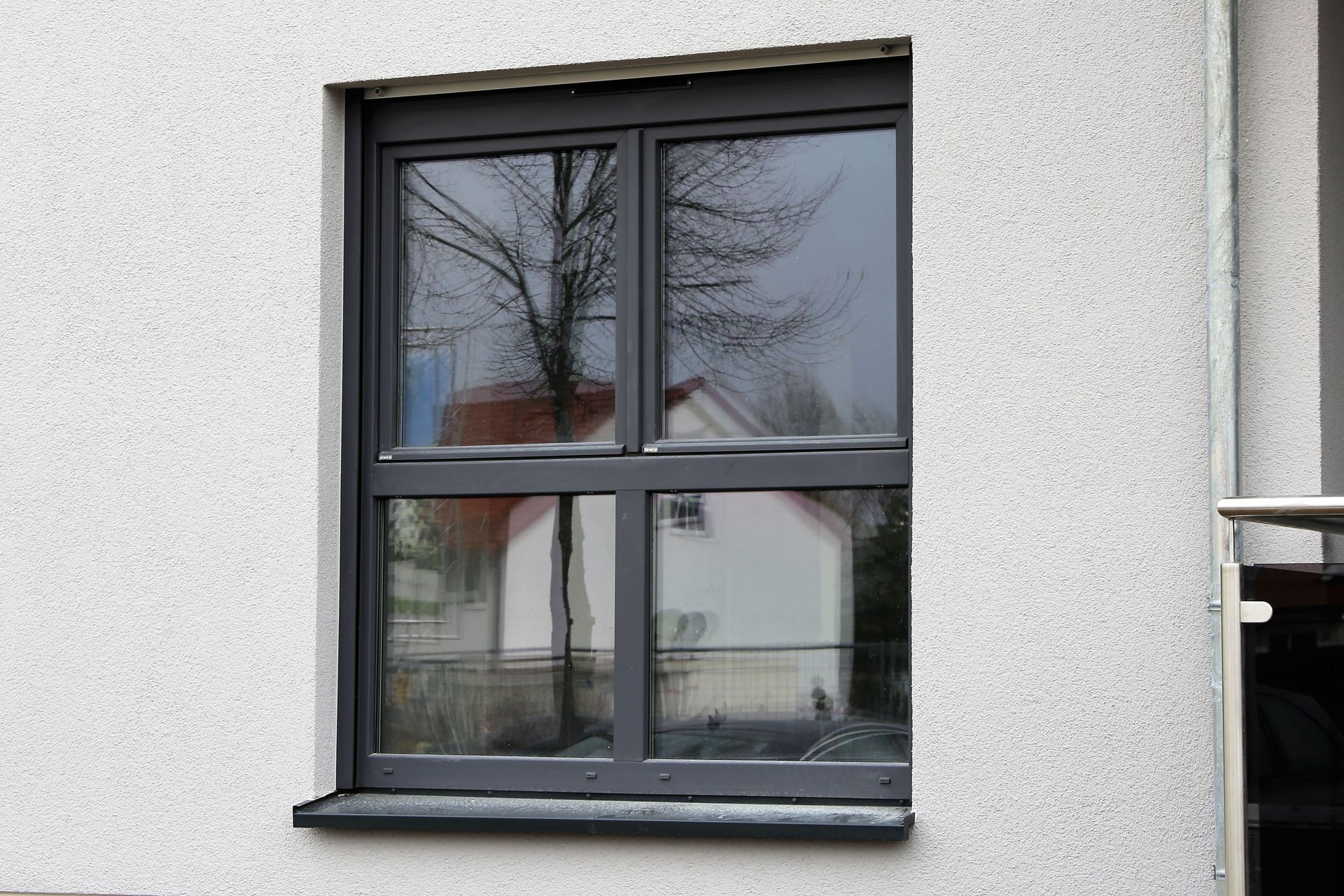 Window with gray frame reflecting a tree and house, set in white textured wall.