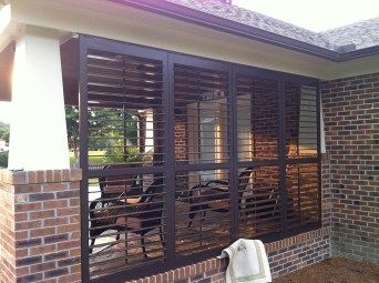 Brown louvered shutters on brick patio; outdoor seating visible behind the shutters; daytime.