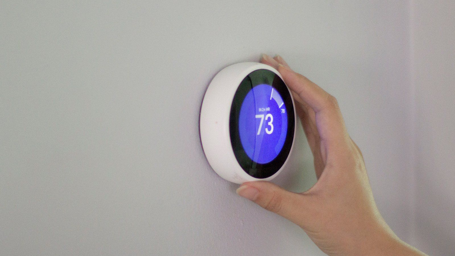 A person is adjusting a smart thermostat on a wall.