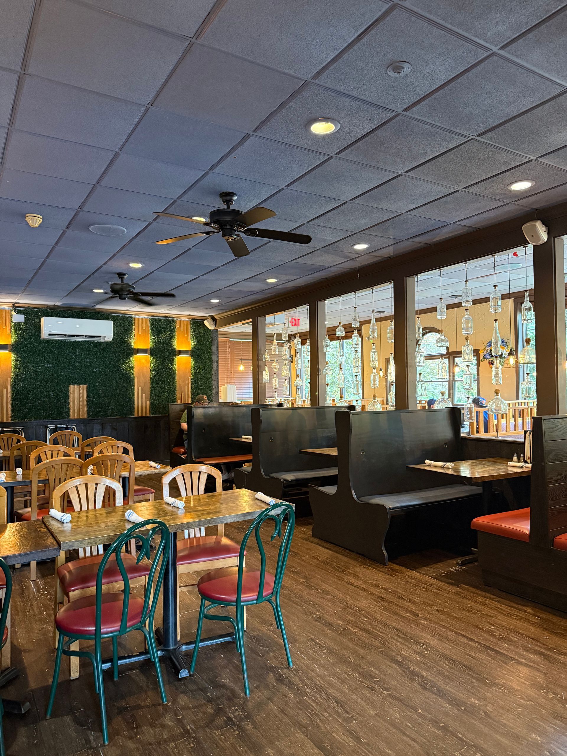 Empty restaurant dining area with wooden tables, booths, and a ceiling fan under purple lighting