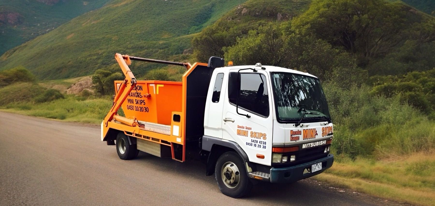 Macedon Ranges Mini Skips truck delivering an orange skip bin on a country road