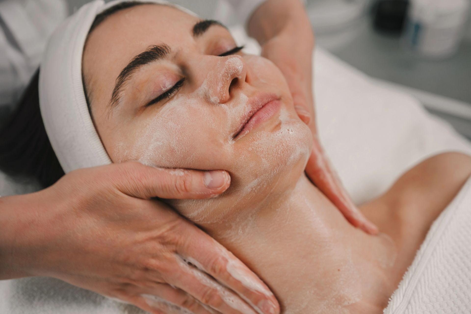Donna che riceve un massaggio al viso con gli occhi chiusi e le mani che applicano la crema.