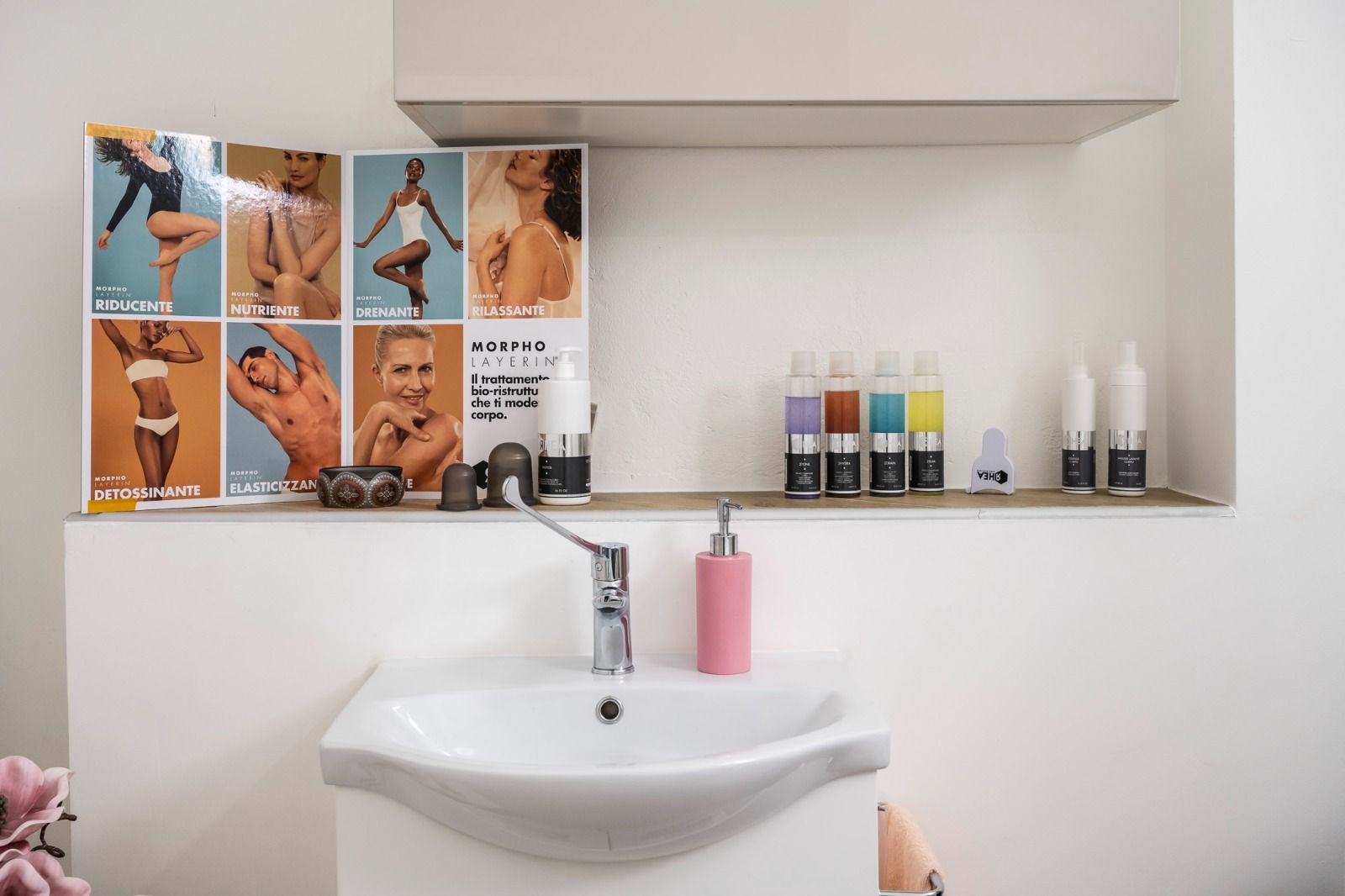 Lavandino del bagno con mensola su cui sono esposti prodotti di bellezza e poster.
