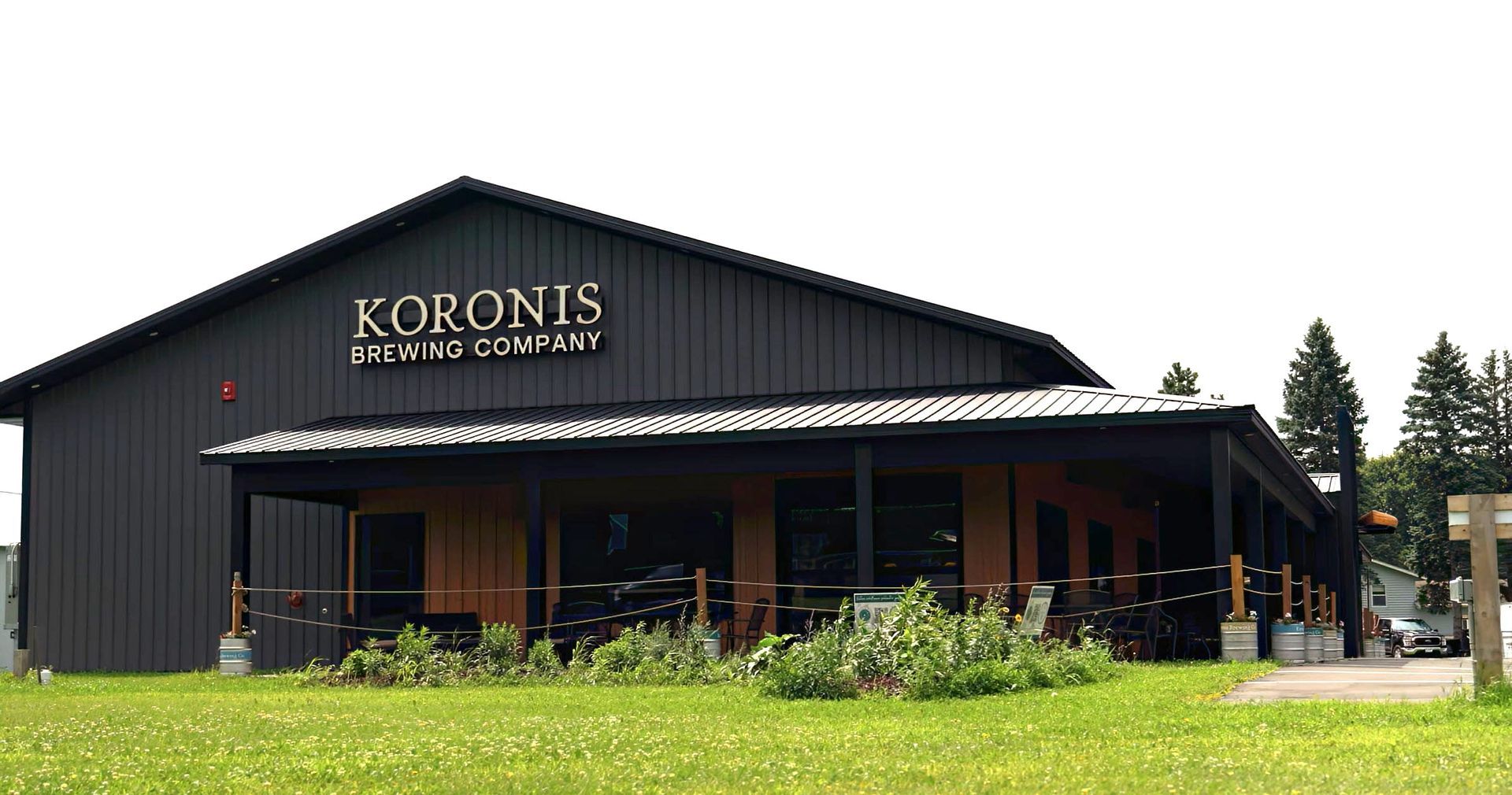 KORONIS Outdoor Concepts storefront with dark siding, covered porch, and green lawn