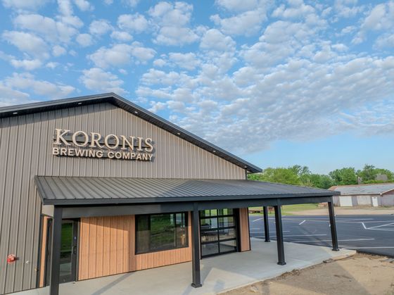 Koronis Brewing Company Viewed from the outside looking, showing out door seating area and overhead doors to event space.