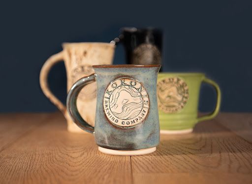Three rustic mugs on a wooden table, with a blue mug in focus in front of a dark background