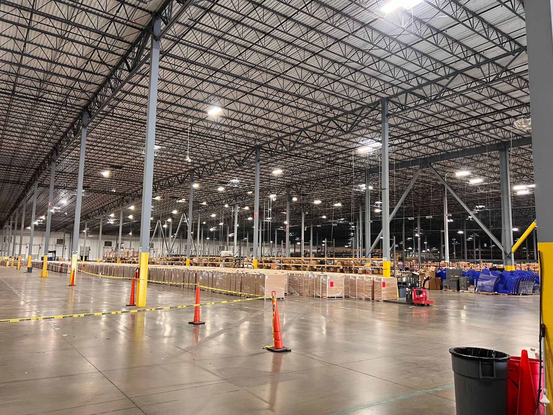 Empty warehouse interior with metal racks, safety cones, and a wet concrete floor