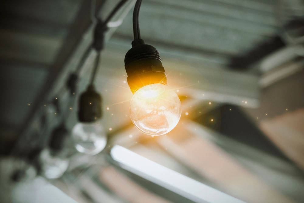 String of clear light bulbs, one glowing brightly, hanging from a dark wire, blurred background.