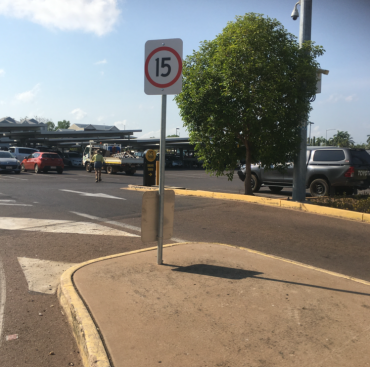 Speed limit sign (15) on a concrete median in a parking lot with cars, and a tree.