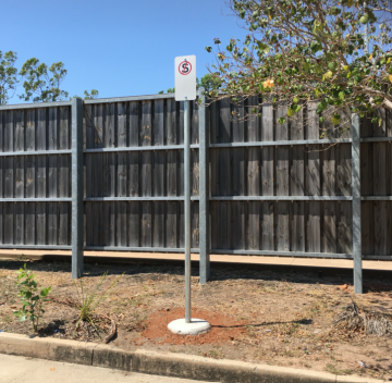 Parking sign with the number 5 on a post, in front of a wooden fence.